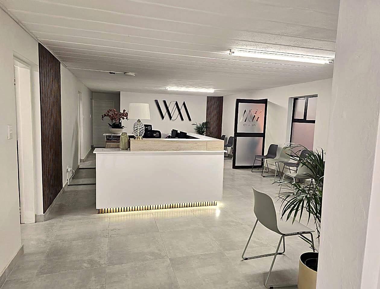 The WillowMed reception desk in white and warm oak, with the practice monogram on the wall